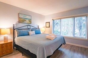 Ein Schlafzimmer mit einem Bett, einem Nachttisch, einem Fenster mit Jalousien und einem Gemälde an der Wand.