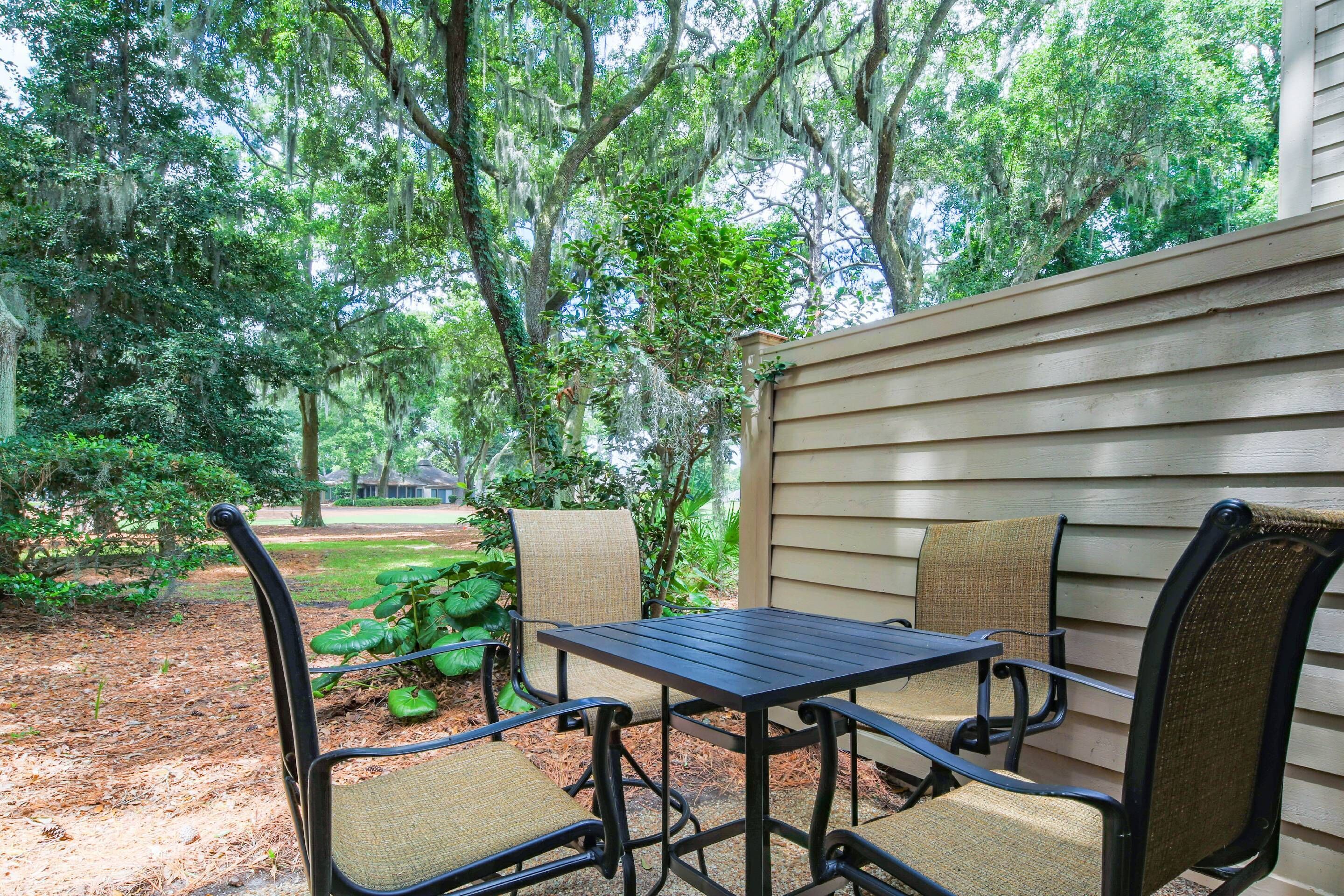 An outdoor patio with a table and chairs, surrounded by trees and greenery.