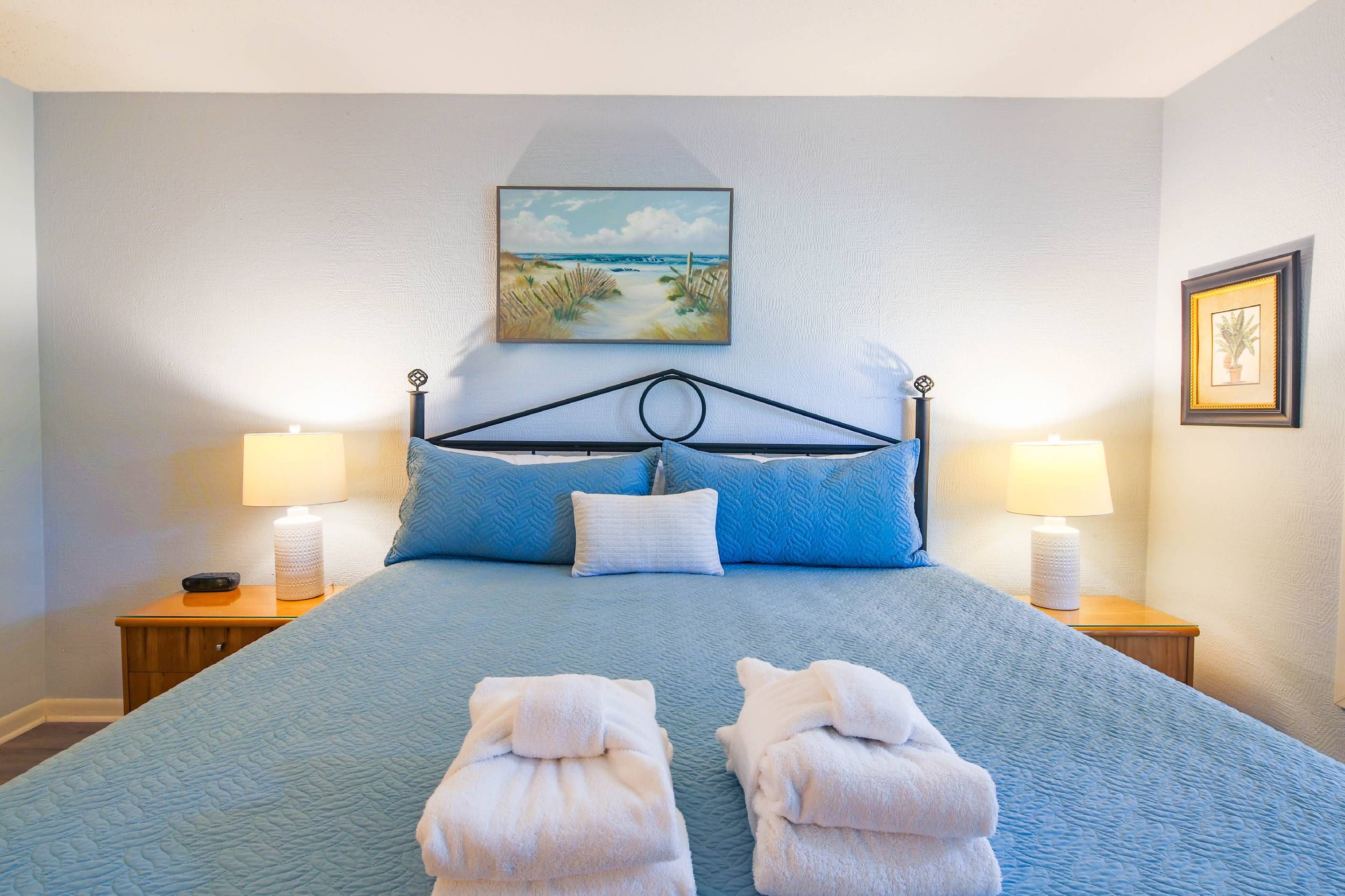 A neatly made bed with a blue quilt, two pillows, and two folded towels on the bed.