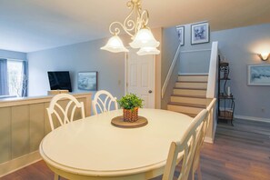 A dining area with a round table, white chairs, a chandelier, and a staircase in the background.