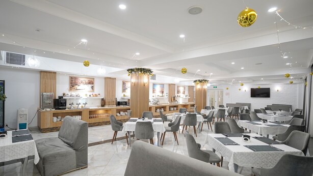 A modern dining area with tables and chairs, a counter with a display, and a television mounted on the wall. - Milan Hotel (Tashkent)