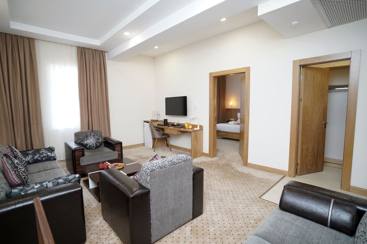A modern hotel room with a living area, a desk, a television, and a separate bedroom.