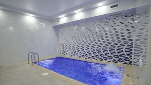 A modern indoor pool with a blue water feature, surrounded by white walls and a decorative lattice. - Milan Hotel (Tashkent)