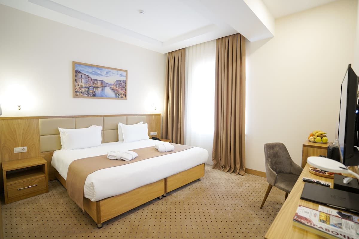 A hotel room with a large bed, a desk with a computer, a chair, a TV, and a painting on the wall.
