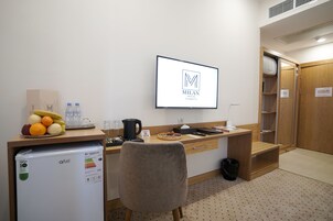 A hotel room with a kitchenette, a desk with a computer, a chair, a bed, and a wardrobe.