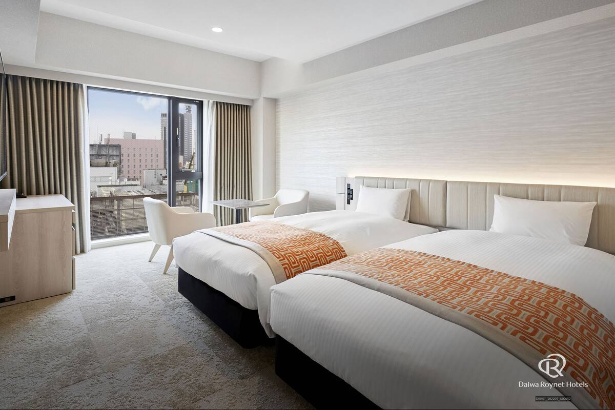 A hotel room with two beds, a desk, and a chair.