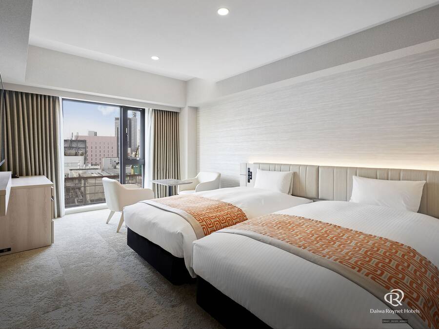 A hotel room with two beds, a desk, and a chair.
