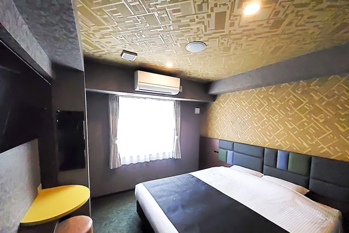 A bedroom with a bed, a window with curtains, an air conditioning unit, and a patterned wall.
