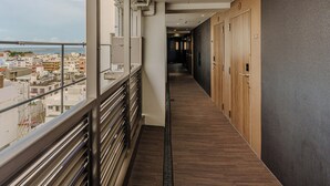 A corridor with a view of the city, wooden doors, and a metal railing. - APA Hotel Naha Airport Wakasa (Naha)