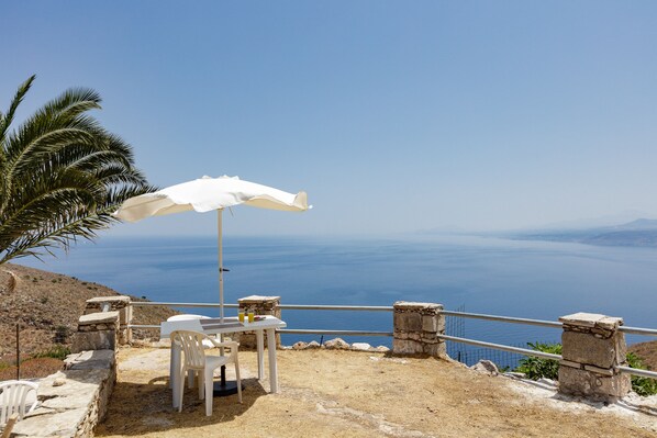 A table with a white umbrella, white chairs, and a view of the sea.