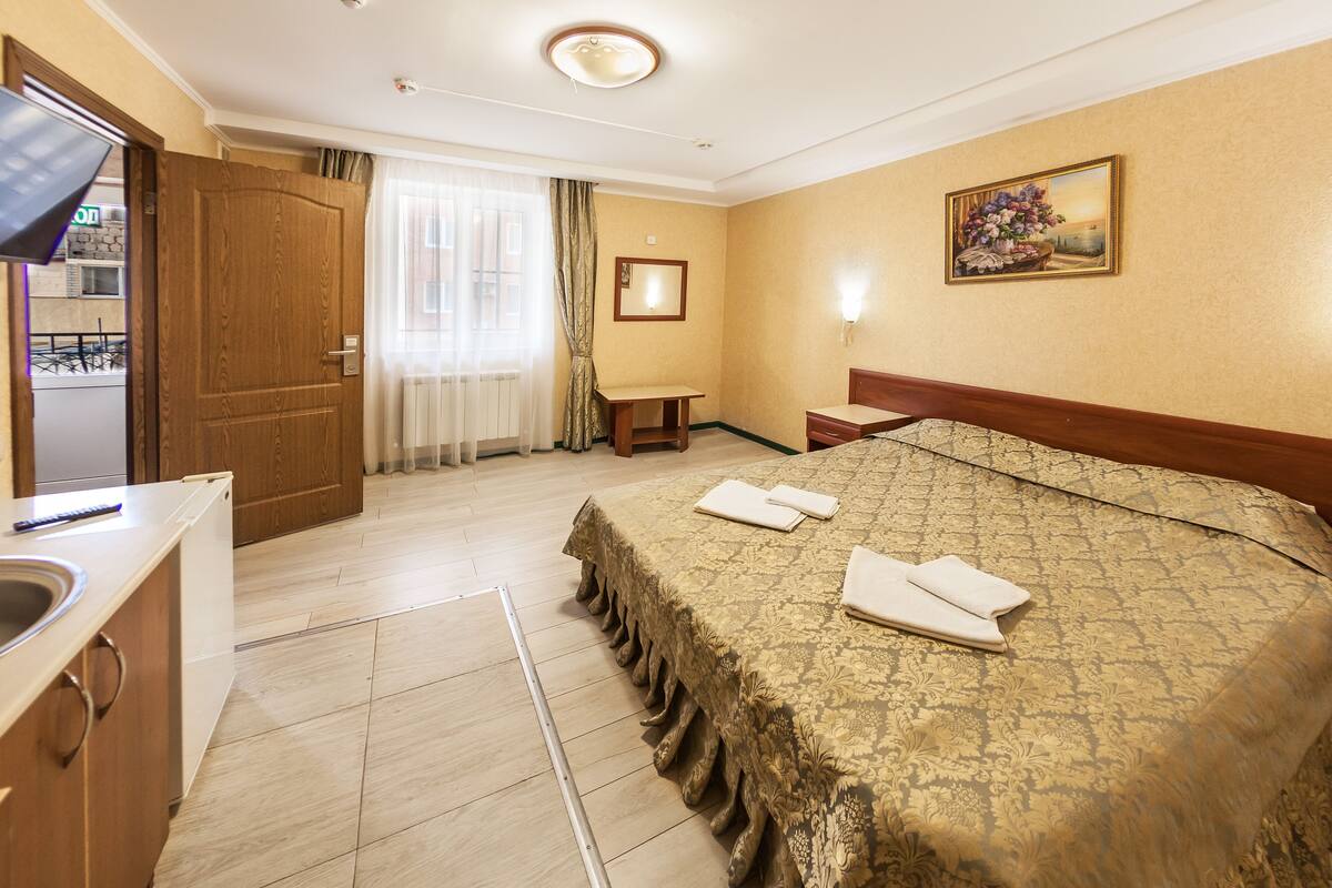 Relax in a stylish room with a neatly made bed, wooden nightstand, and large window with sheer curtains.