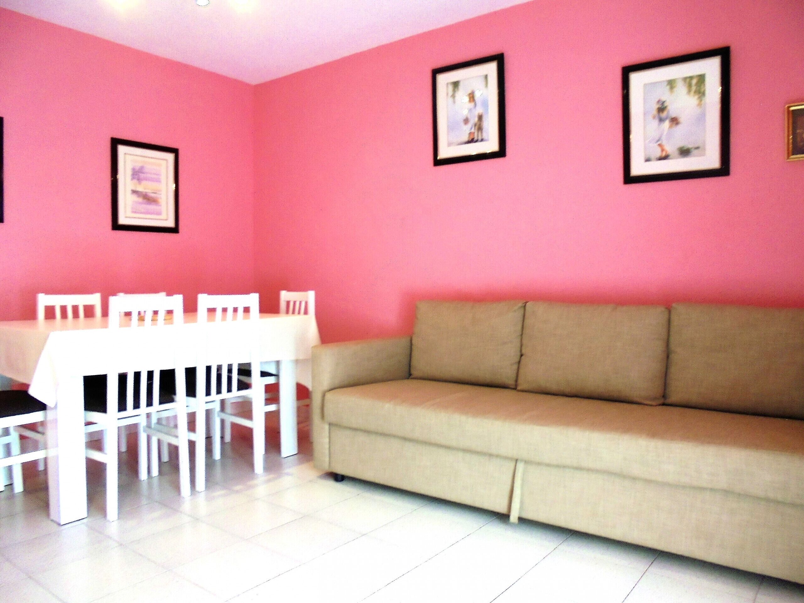 A room with a beige sofa, white chairs, and a table against a pink wall.
