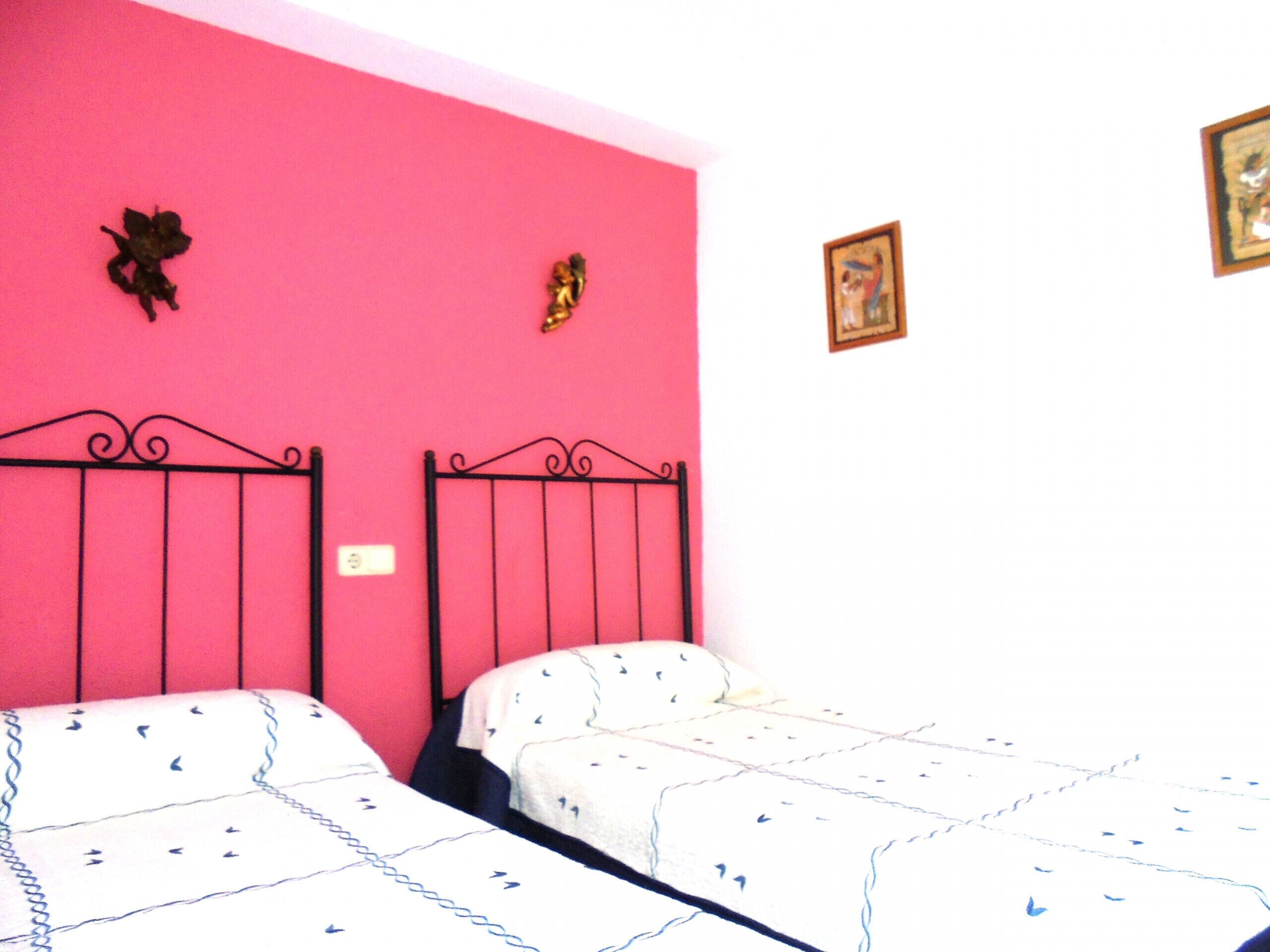 A room with two beds, pink walls, and decorative angel figures.