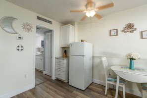 A compact kitchen with a refrigerator, a dining table with a chair, and a ceiling fan.