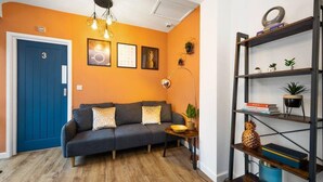 A living room with a blue door, a gray sofa, a wooden floor, a bookshelf, and a wall with framed pictures. - 7 bed house| Sleeps 14 | ENSUITE |Free HS WIFI | TVs in rooms | CITY CENTRE | Inspire Homes (Coventry)