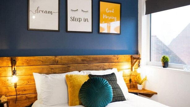 A bedroom with a wooden headboard, a bed with white and yellow pillows, and three framed motivational quotes on the wall. - 7 bed house| Sleeps 14 | ENSUITE |Free HS WIFI | TVs in rooms | CITY CENTRE | Inspire Homes (Coventry)