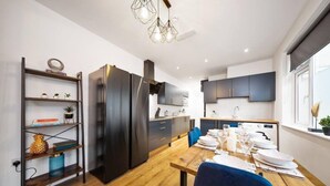 A modern kitchen with dark cabinets, a central island, and a dining area with blue chairs. - 7 bed house| Sleeps 14 | ENSUITE |Free HS WIFI | TVs in rooms | CITY CENTRE | Inspire Homes (Coventry)