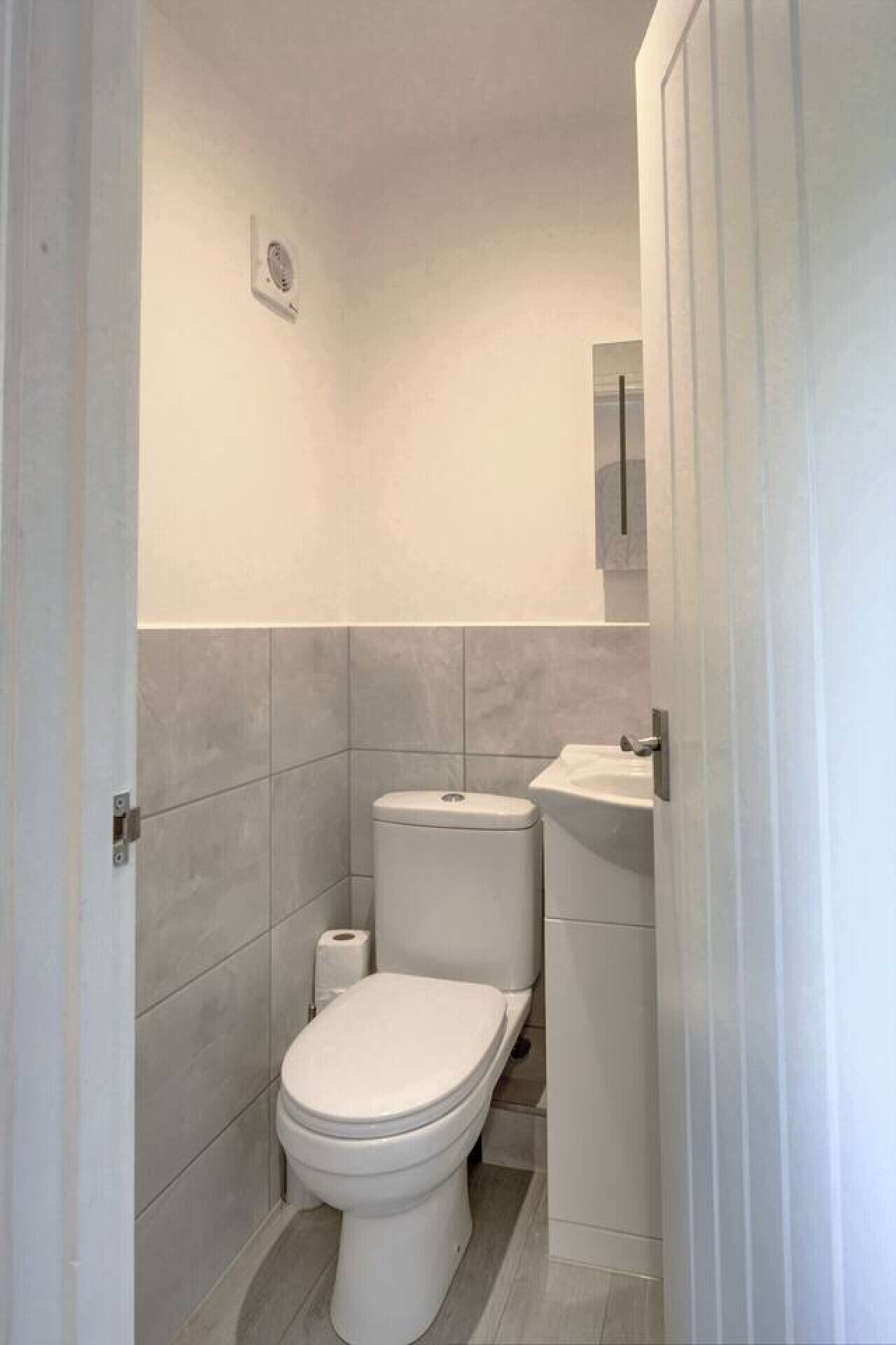 Ein kleines, modernes Badezimmer mit Toilette, Waschbecken und einer Toilettenpapierrolle.