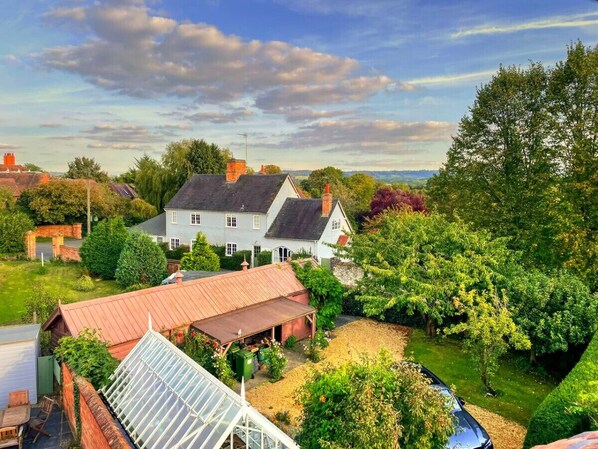 Une grande maison avec un toit rouge, une serre et un jardin bien entretenu.