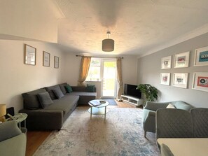Una sala de estar con un sofá, sillones, una mesa de centro y una televisión.