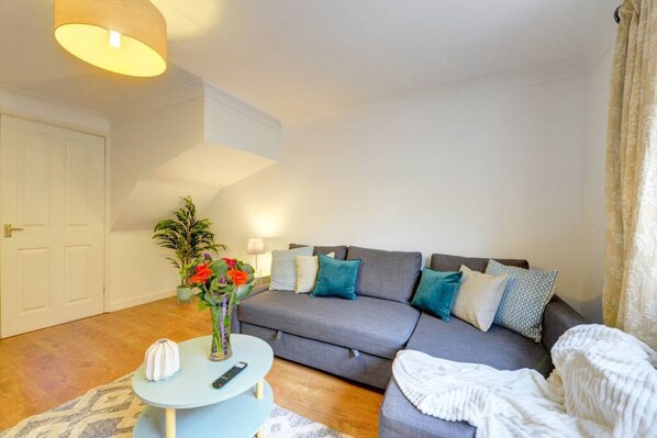 A living room with a grey sofa, a round coffee table, a white door, and a plant with red flowers.