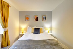 A hotel room with a bed, two bedside tables, a window with curtains, and three wall-mounted artworks.