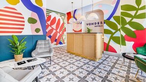 Moderni hotellin aula, jossa on vastaanottotiski, oleskelualue ja värikäs, abstrakti seinätaide.