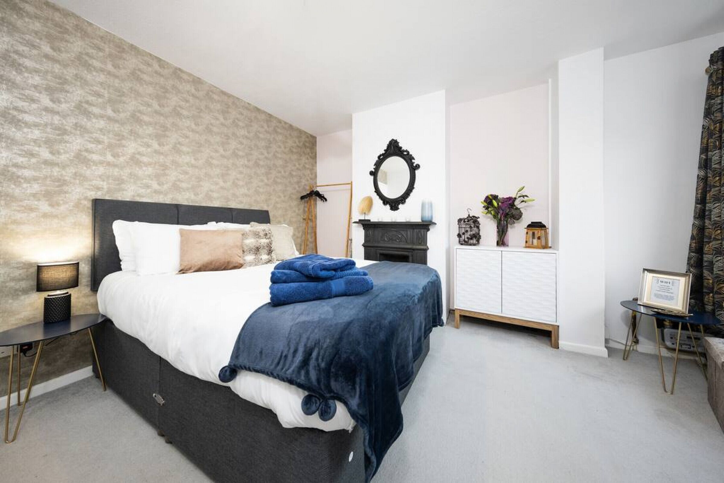 A bedroom with a large bed, a nightstand, a dresser, a mirror, and a small table with a framed picture.
