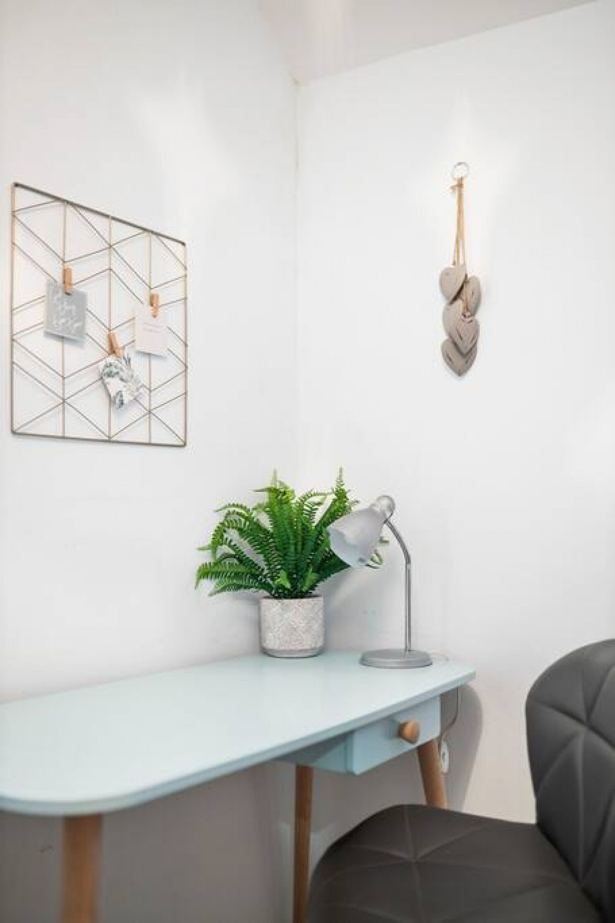 Ein Eckzimmer mit Schreibtisch, Blumentopf, Wandleuchte und einem Wandbild mit geometrischen Formen.
