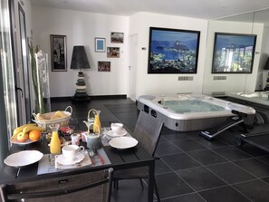 Ett modernt rum med ett matbord dukat för frukost, ett bubbelbad och utsikt över staden.