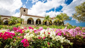 A building with a tower, arched windows, and a garden with colorful flowers.