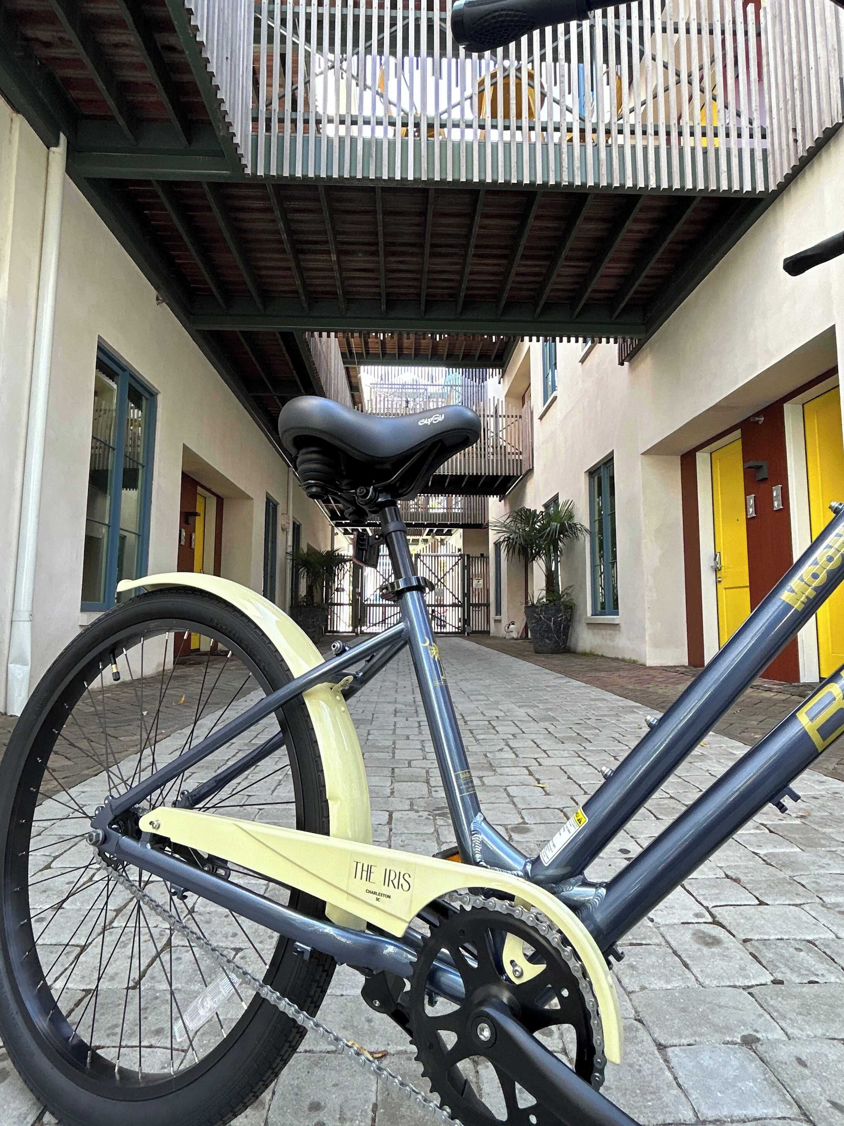 Een fiets geparkeerd op een geplaveid straatje, met een metalen hekwerk en een gele deur op de achtergrond.