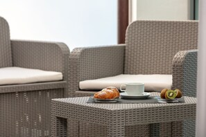 Wicker furniture with cushions, a plate with a pastry and kiwi, and a cup on a table. - Capotesta Luxury Rooms (Santa Teresa di Gallura)