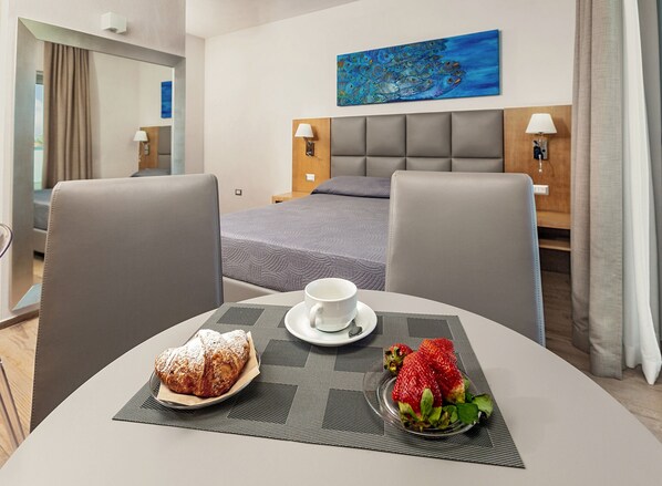 A hotel room with a bed, a dining table with a cup and pastries, and a painting on the wall. - Capotesta Luxury Rooms (Santa Teresa di Gallura)