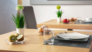 Ett matbord med en tallrik, ett glas, en skiva kiwi, en croissant och en liten krukväxt.