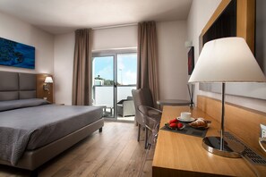 A hotel room with a bed, a desk with a lamp, a chair, a table with food and a cup, and a painting on the wall. - Capotesta Luxury Rooms (Santa Teresa di Gallura)