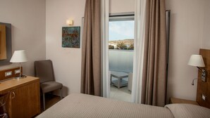 Ett hotellrum med en säng, en stol, ett skrivbord, en lampa, en tavla och en balkong med utsikt.