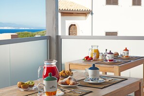 A breakfast table with croissants, a glass of orange juice, and a pitcher of red juice on a balcony overlooking a coastal view. - Capotesta Luxury Rooms (Santa Teresa di Gallura)