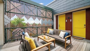 A wooden deck with wicker furniture, a table with a tray of food, and a yellow door. - The Iris, Signature Suite (Charleston)