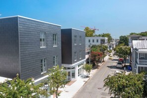 A modern building with a flat roof and large windows, situated on a street with trees and parked cars.