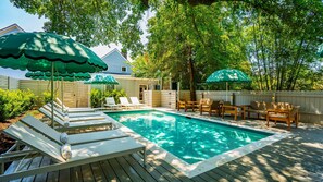 A backyard with a swimming pool, lounge chairs, and umbrellas. - The Iris, Signature Suite (Charleston)