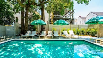 A swimming pool with lounge chairs and umbrellas, surrounded by trees and a fence.