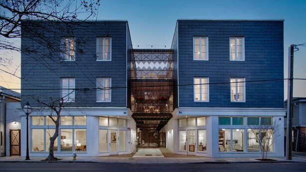 A modern two-story building with a central entrance, large windows, and a visible outdoor seating area. - The Iris, Signature Suite (Charleston)