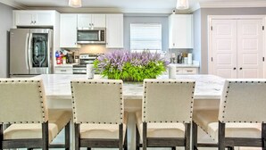 Uma cozinha moderna com armários brancos, eletrodomésticos de aço inoxidável e uma ilha central com um arranjo floral.
