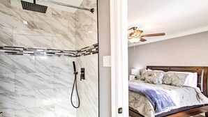 Uma casa de banho com chuveiro e um quarto com cama e ventoinha no teto.