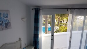 A bedroom with a bed, a nightstand, a wall-mounted lamp, and a view of a swimming pool through a glass door. - Holiday Home "Casa Los Pinos" with Sea View, Shared Pool, Balcony, A/C & Wi-Fi (Sitio de Calahonda)