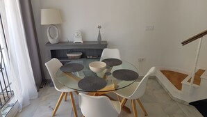 A dining area with a glass table, white chairs, and a decorative cat figurine on the wall. - Holiday Home "Casa Los Pinos" with Sea View, Shared Pool, Balcony, A/C & Wi-Fi (Sitio de Calahonda)