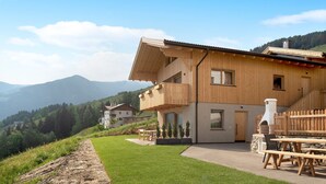 Uma casa de madeira com varanda, forno de pedra e vista para as montanhas.