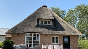 A thatched-roof house with a brick exterior, large windows, and outdoor seating. - Reet Kate|3SZ|Sauna|Garding in St. Peter-Ording (Garding, Kirchspiel)