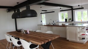 A modern kitchen with a wooden dining table and white chairs, featuring a black pendant light, white cabinets, and a window with a view of greenery. - Reet Kate|3SZ|Sauna|Garding in St. Peter-Ording (Garding, Kirchspiel)